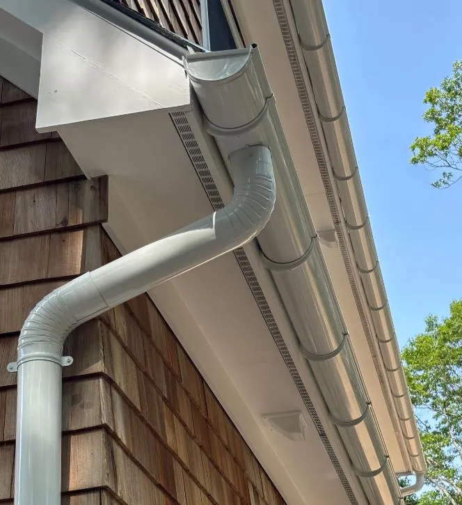 White downspout connected to a half-round gutter on a cedar-shake wall